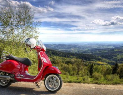 red Italian vespa motorcycle in the hilly countryside with blue sky and white clouds - travel experience by Timeless Tuscany tour operator