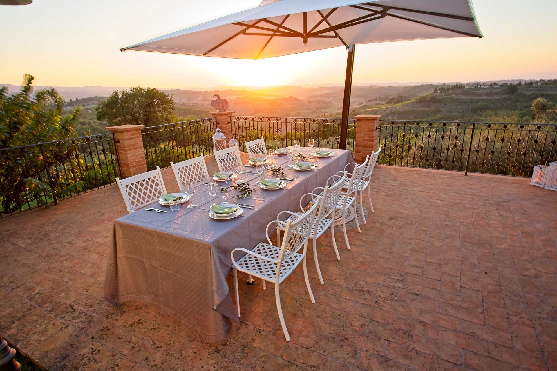 Italian dinner at Villa Bellavista on terrace at sunset; table with grey table cloth; white chairs and umbrella; Chianti hills view - villa rentals by Timeless Tuscany tour operator