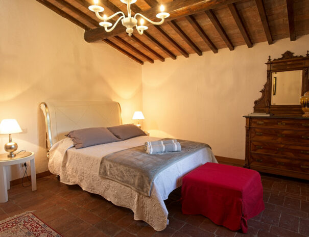 Italy Villa Bellavista Certaldo Chianti; king-size bedroom; red pouf; persian carpet; wooden beams ceiling with chandelier - villa rentals by Timeless Tuscany tour operator