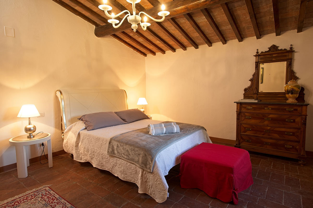 Italy Villa Bellavista Certaldo Chianti; king-size bedroom; red pouf; persian carpet; wooden beams ceiling with chandelier - villa rentals by Timeless Tuscany tour operator