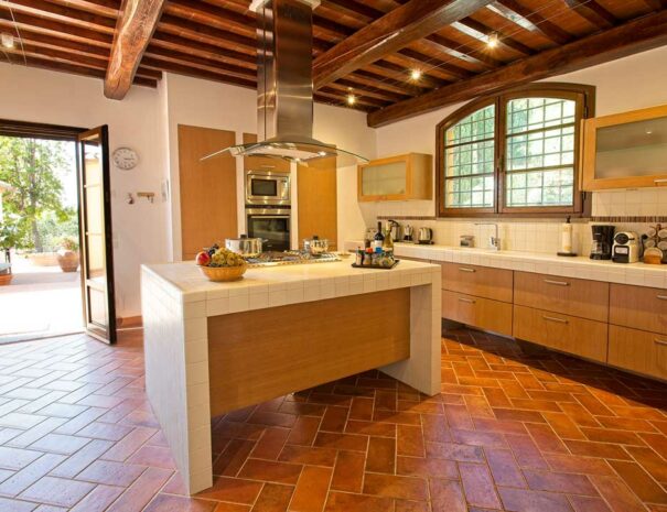 Italy Villa Bellavista Certaldo Chianti; kitchen island with cook top; door to garden and window above cabinets; wooden beams ceiling with lighting - villa rentals by Timeless Tuscany tour operator